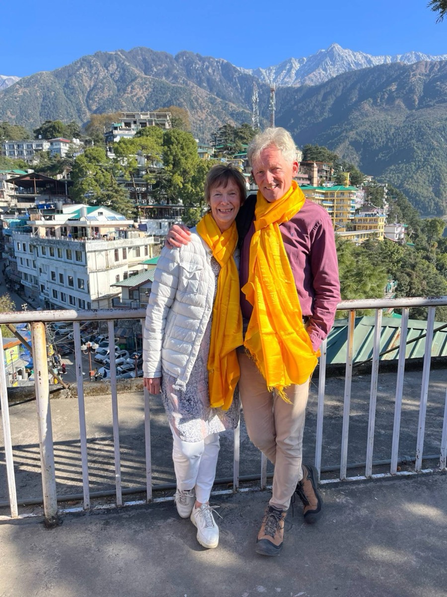 Jette Kristiansen og Uffe Kjærulff med gule tørklæder foran bjergene i Dharamsala